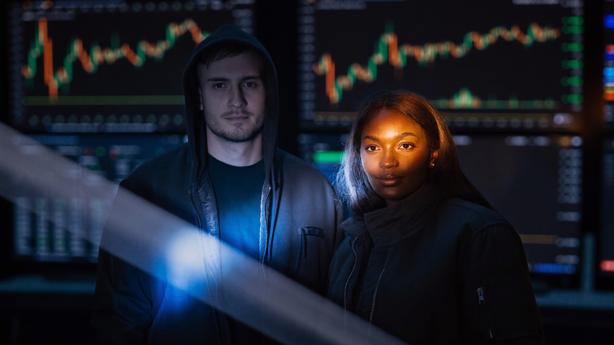 Two traders in a dark trading room, lit by a prismatic beam of blue and orange light